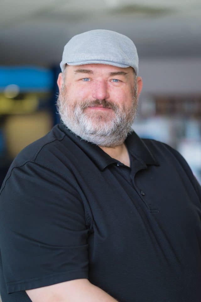 Headshot of a white man with a beard wearing a cap and a black polo shirt